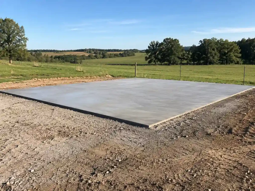 Freshly poured concrete pad on a rural property prepared for a future metal building installation