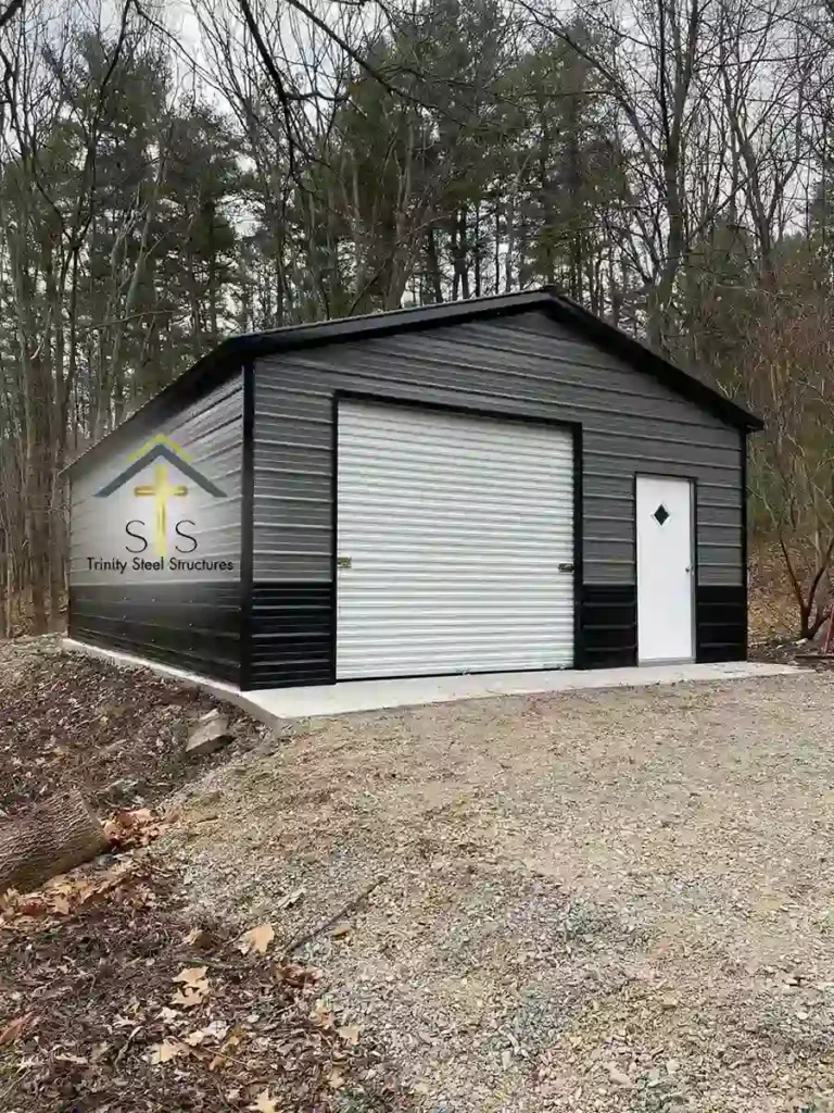 Gray and black metal garage by Trinity Steel Structures with a white roll-up door and walk-in door